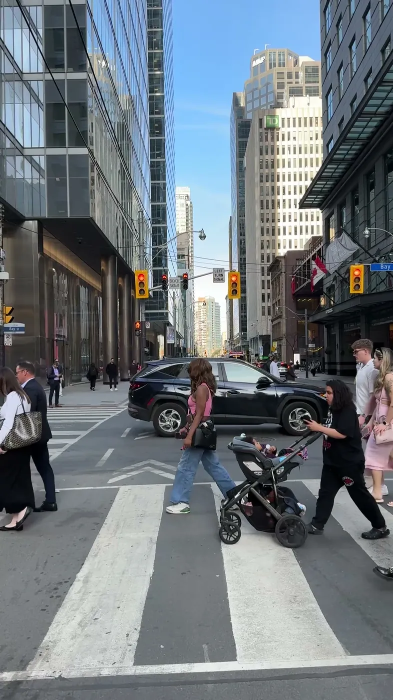 Adults and a child in a stroller crossing a downtown Toronto street