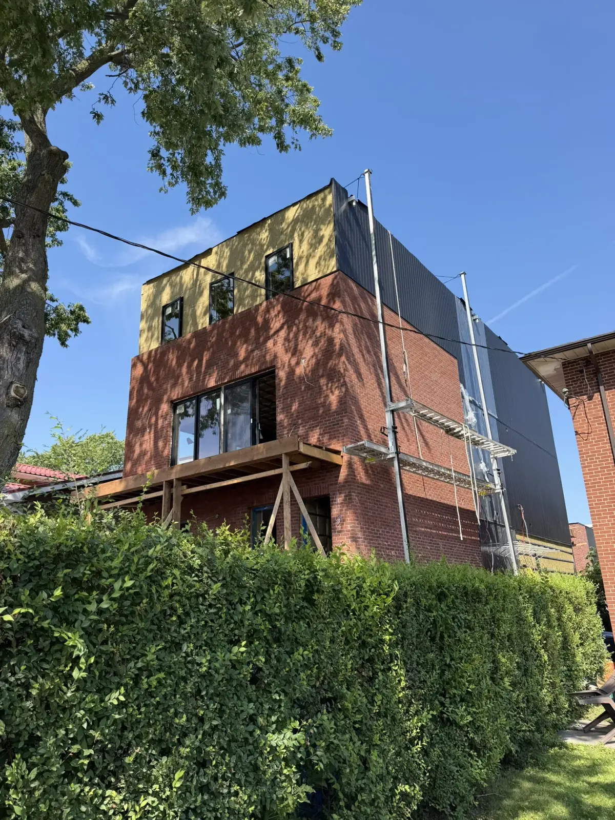 Brick exterior, windows and scaffolding beneath a mature tree canopy during construction
