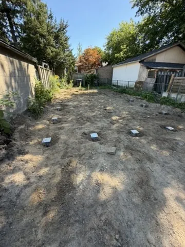 Cleared rear portion of a Toronto lot between fences and neighbouring buildings, with trees beyond